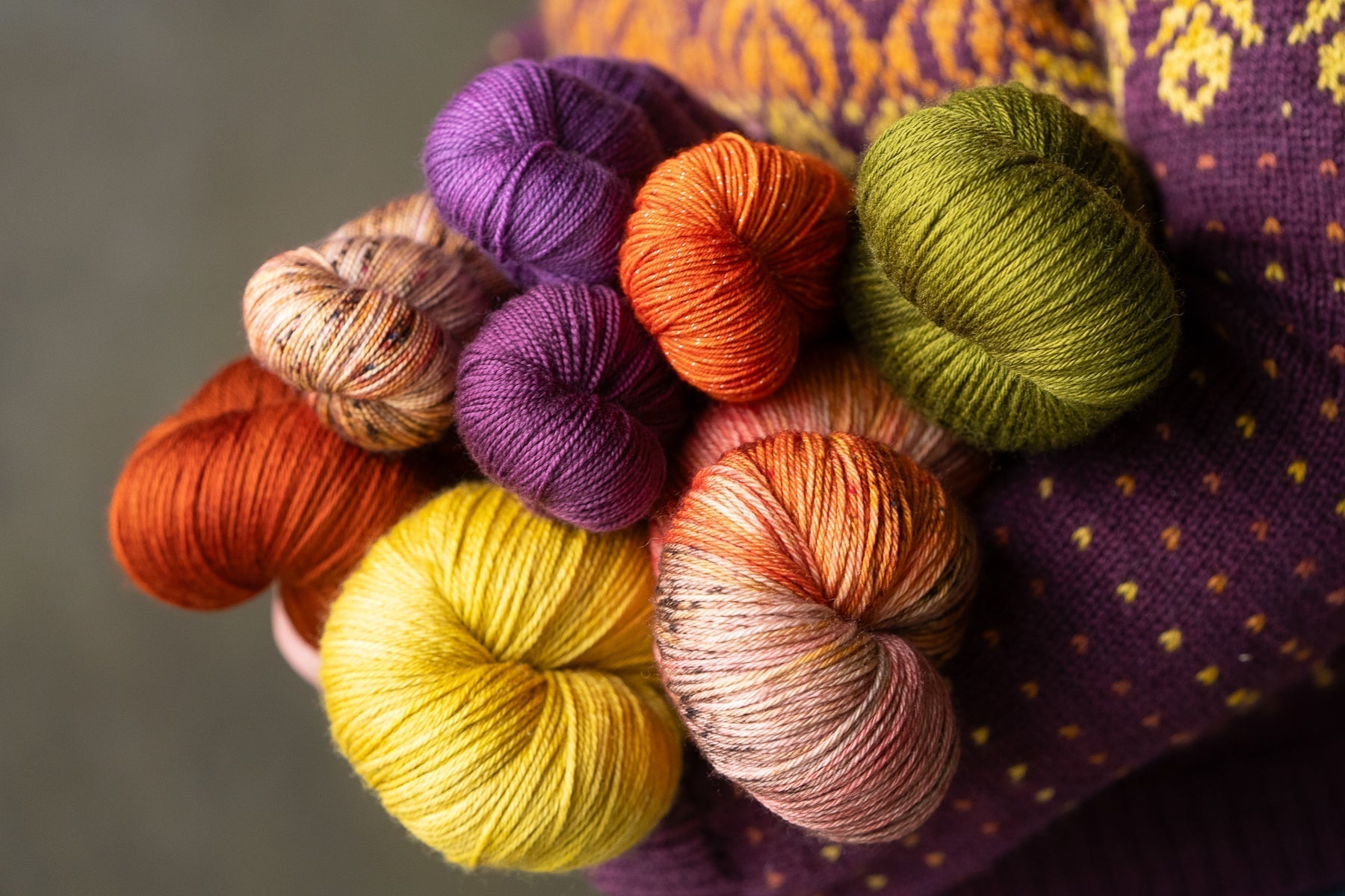 A person wearing a sweater holds an armful of yarn in fall colors