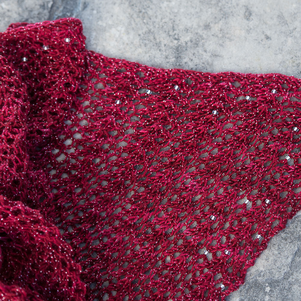 Close up of red lacy shawl laying on stone.
